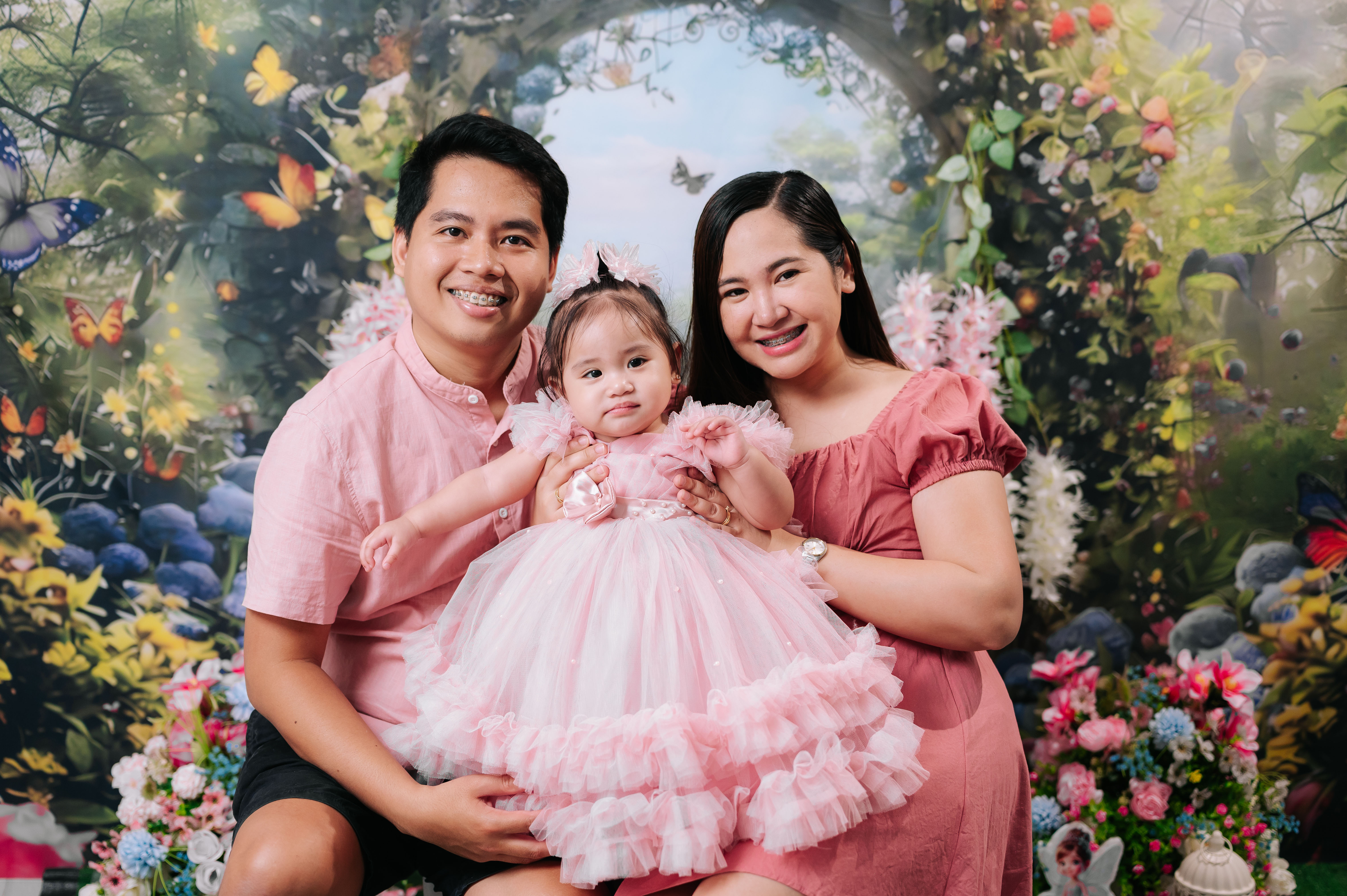 Amara Izabella with her parents, dressed in pink in a fairy garden setting