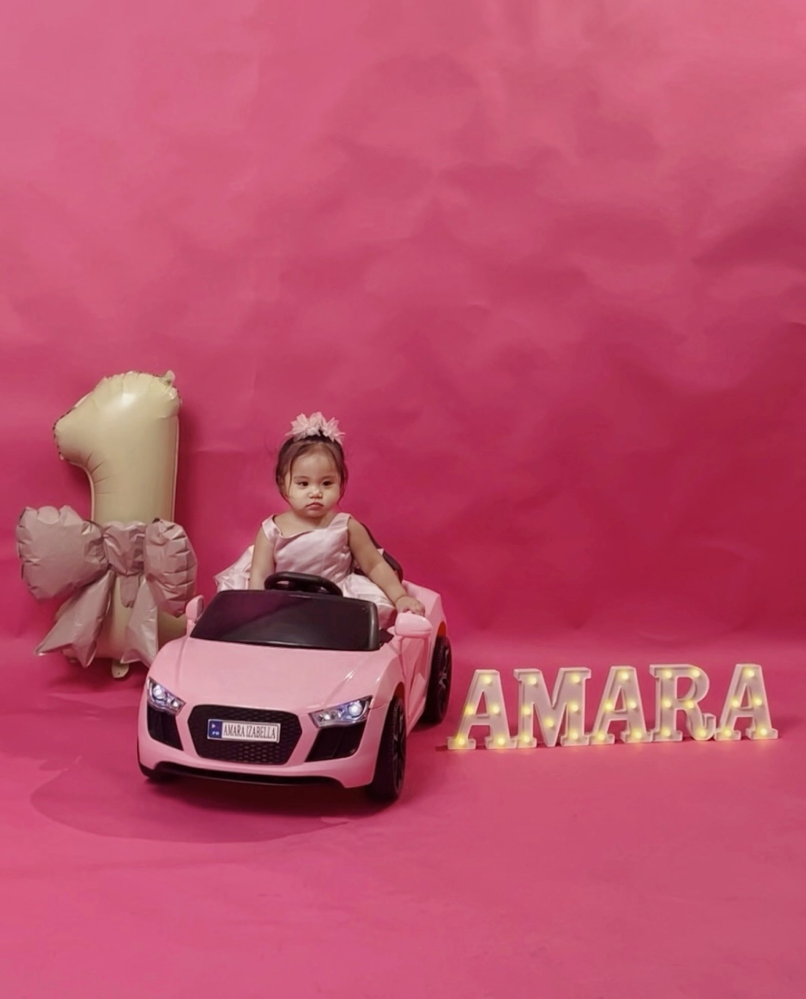 Amara in a pink toy car in her fairy garden setting